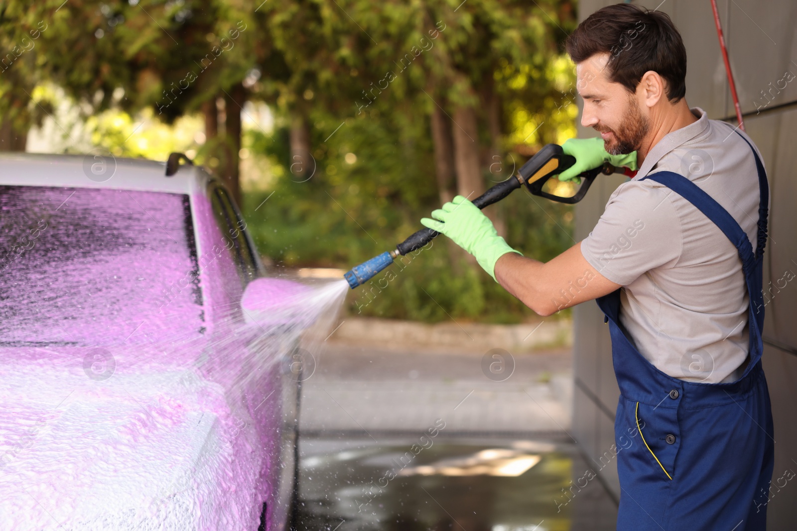 Photo of Worker washing auto with high pressure water jet at outdoor car wash