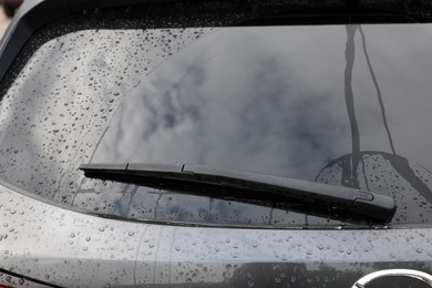 Car wiper cleaning water drops from rear windshield glass, closeup