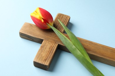 Photo of Easter - celebration of Jesus resurrection. Wooden cross and tulip on light blue background, closeup