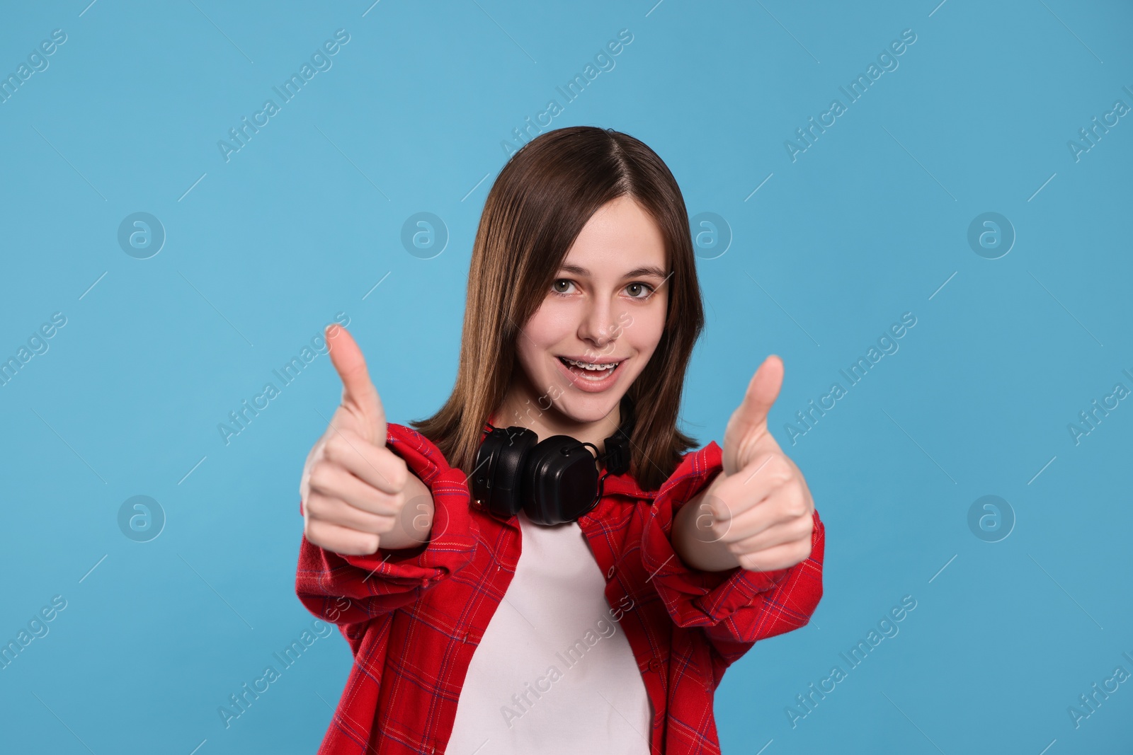 Photo of Portrait of smiling teenage girl showing thumbs up on light blue background