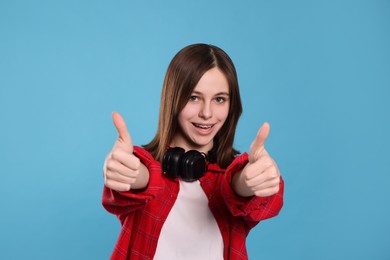 Photo of Portrait of smiling teenage girl showing thumbs up on light blue background