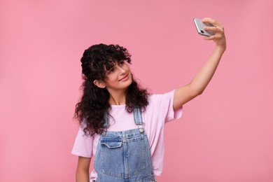 Beautiful young woman taking selfie on pink background