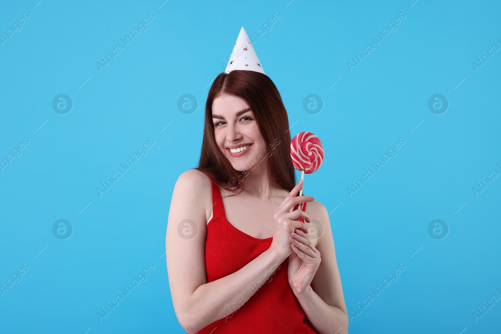 Photo of Happy woman in party hat with lollipop on light blue background