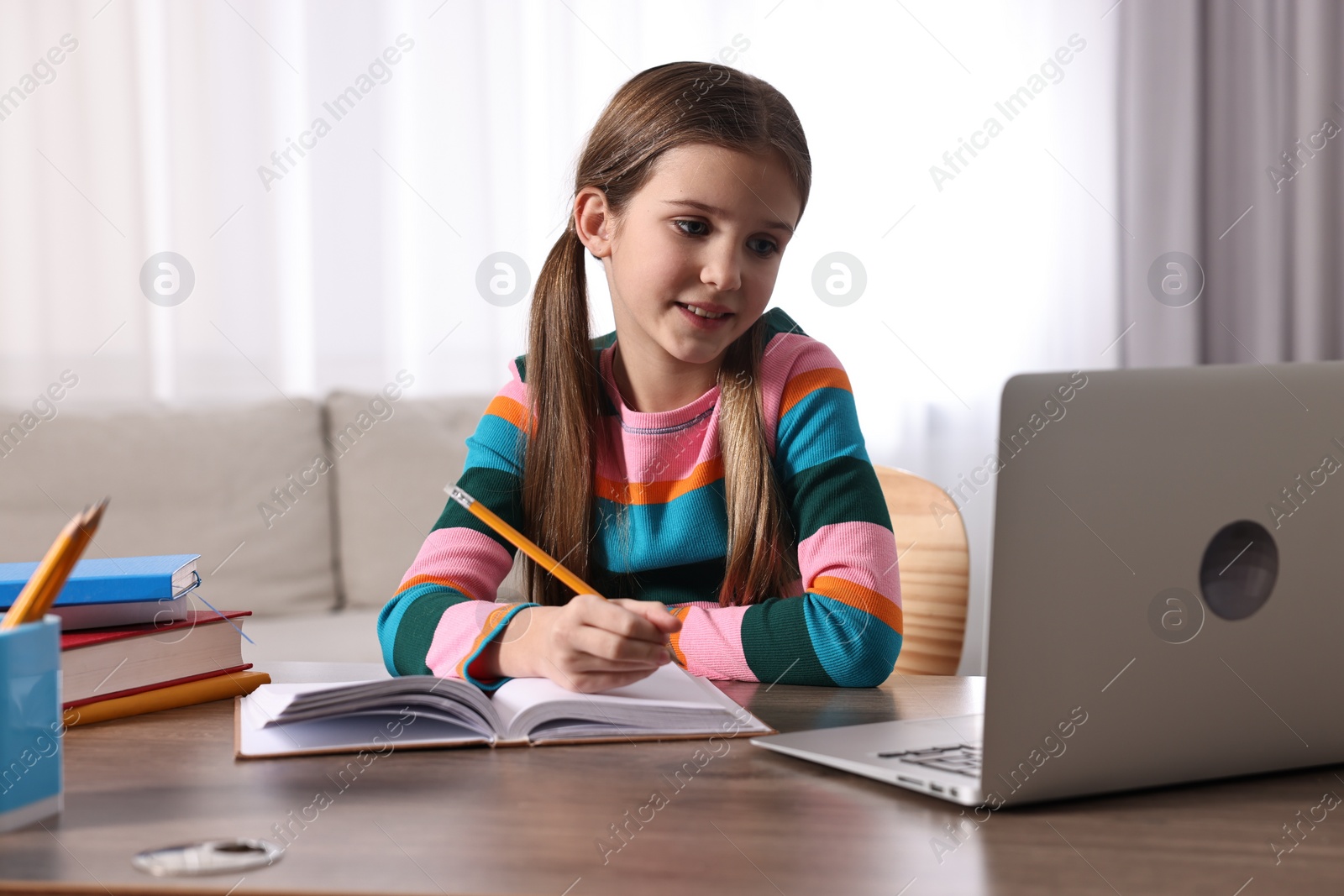 Photo of E-learning. Cute girl taking notes during online lesson at table indoors