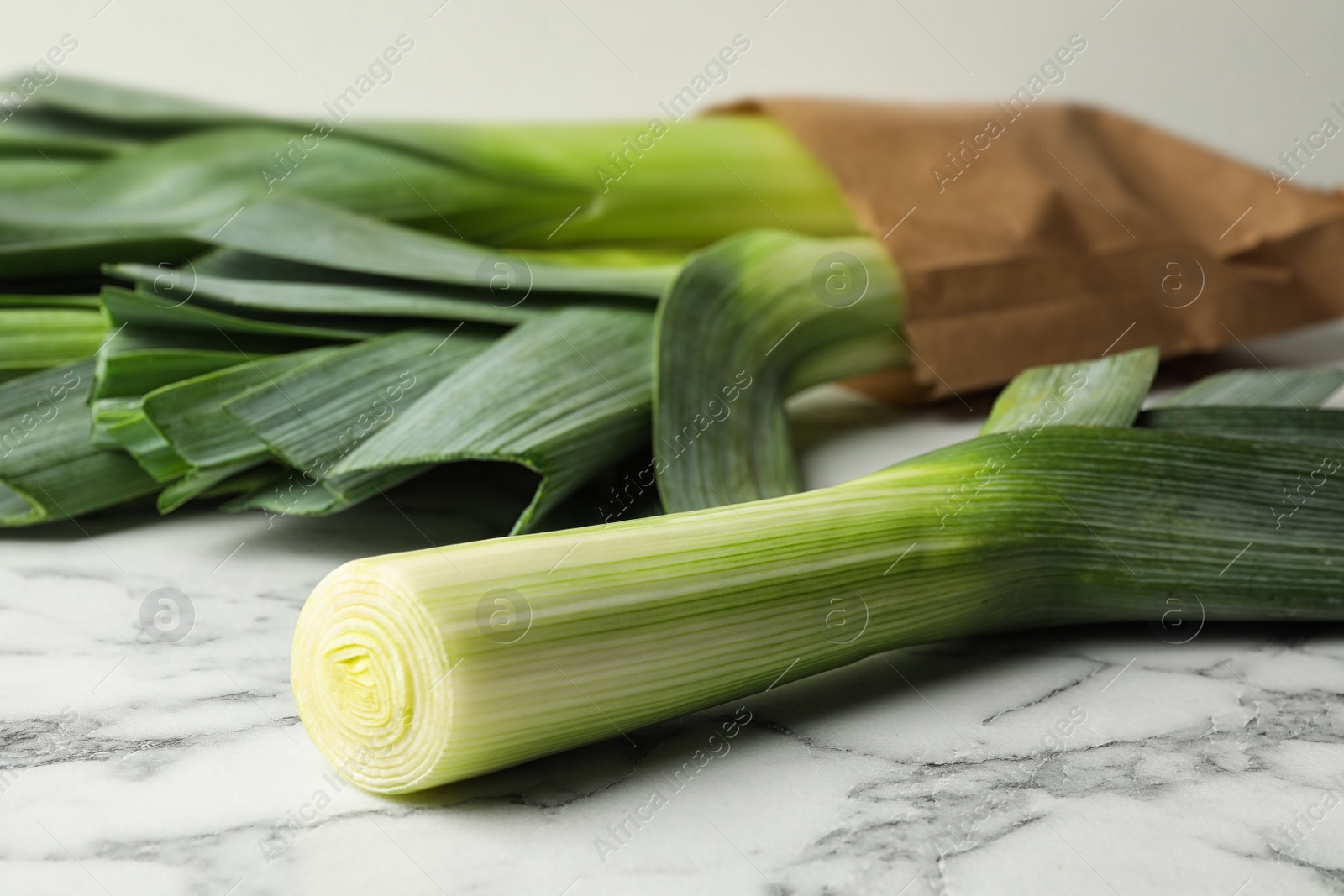 Photo of Fresh raw leeks on marble table, closeup. Ripe onion