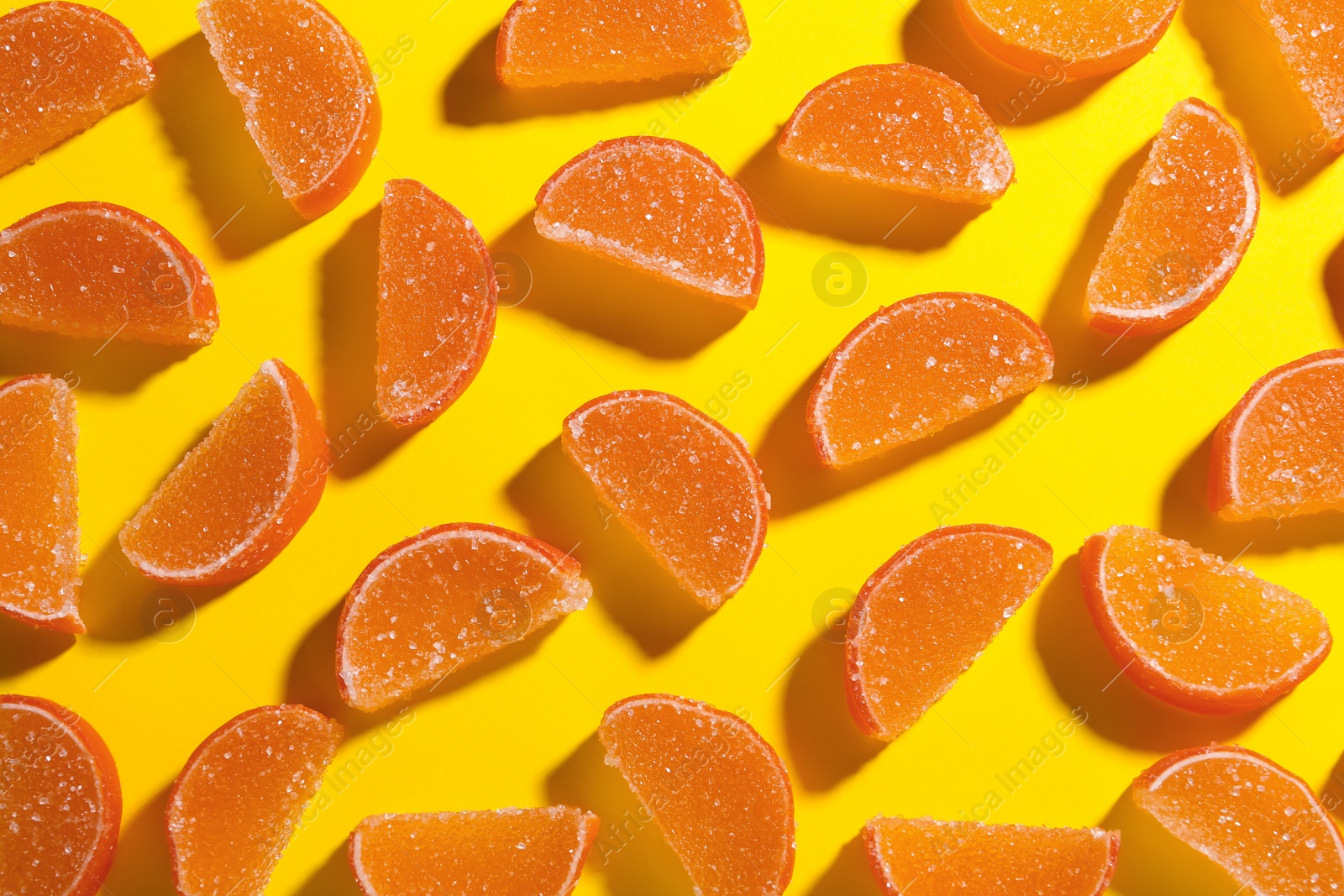 Photo of Delicious orange marmalade candies on yellow background, flat lay