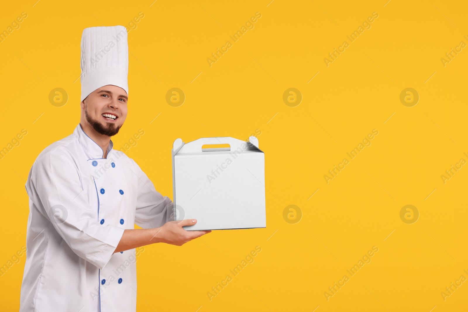 Photo of Happy professional confectioner in uniform holding cake box on yellow background. Space for text
