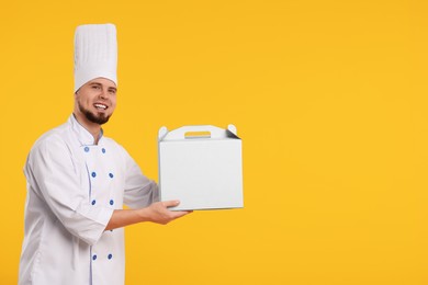 Photo of Happy professional confectioner in uniform holding cake box on yellow background. Space for text