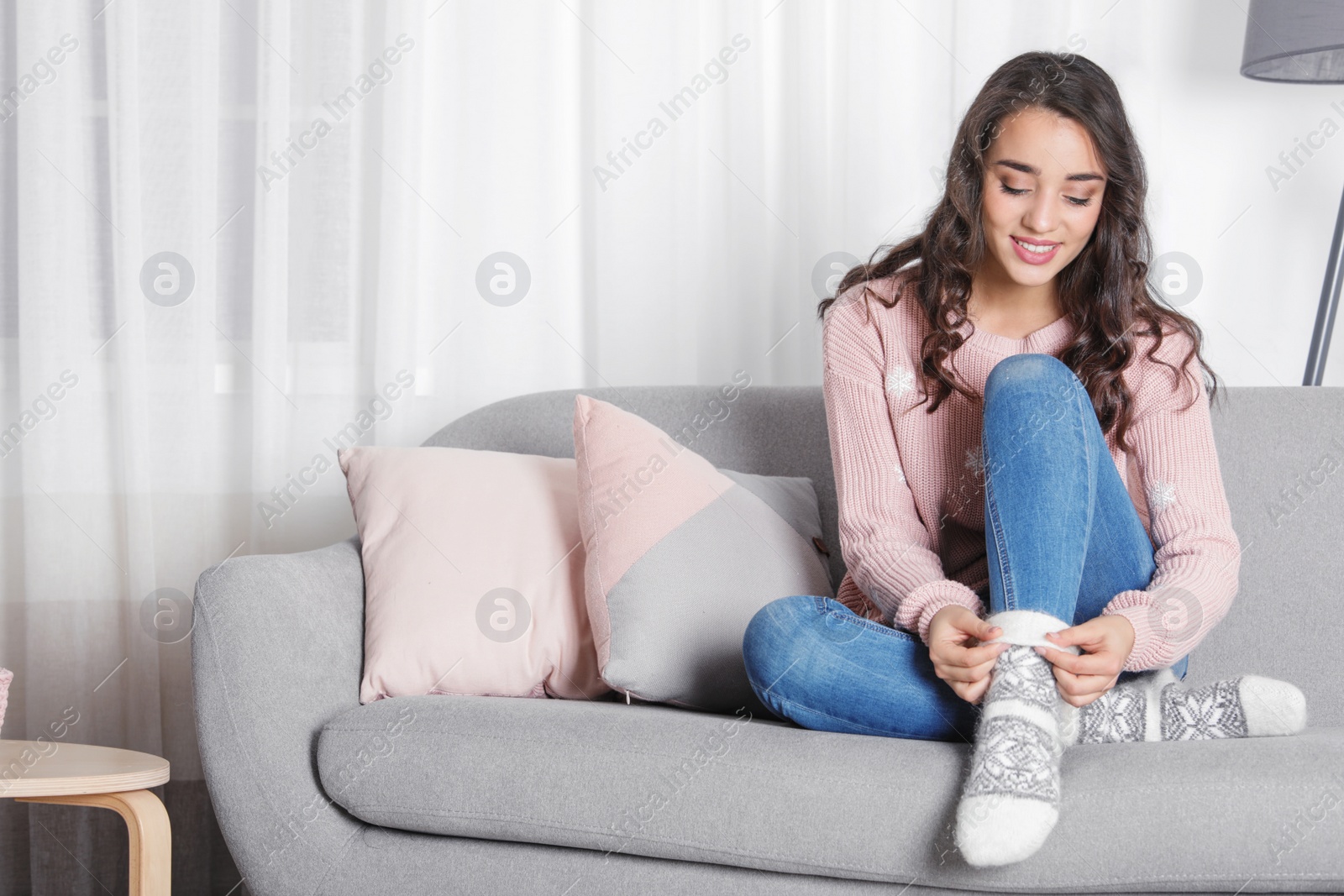 Photo of Young woman in warm sweater sitting on sofa at home. Space for text