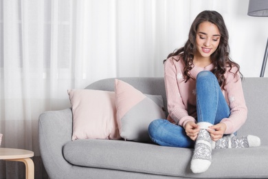 Young woman in warm sweater sitting on sofa at home. Space for text