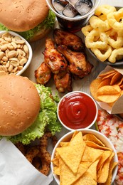 Photo of Chips, burgers and other fast food on white wooden table, flat lay