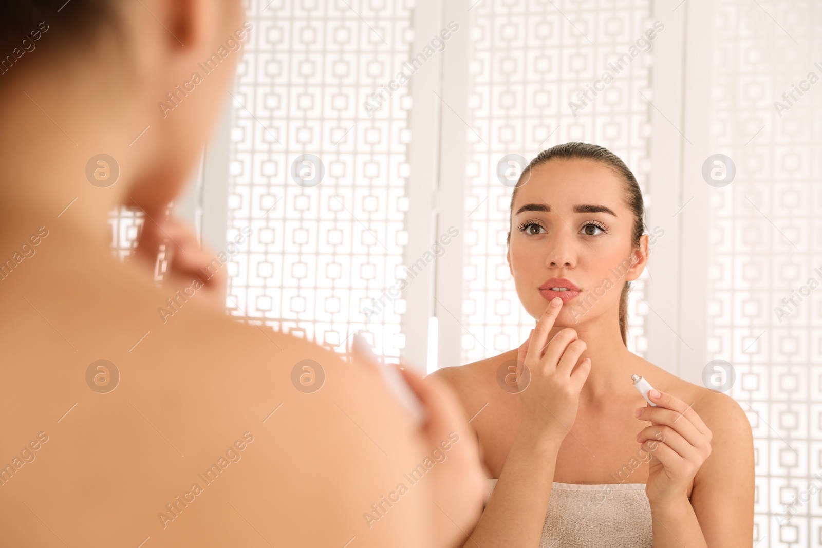 Photo of Woman with herpes applying cream on lips in front of mirror at home