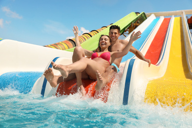 Photo of Happy couple on slide at water park, low angle view. Summer vacation