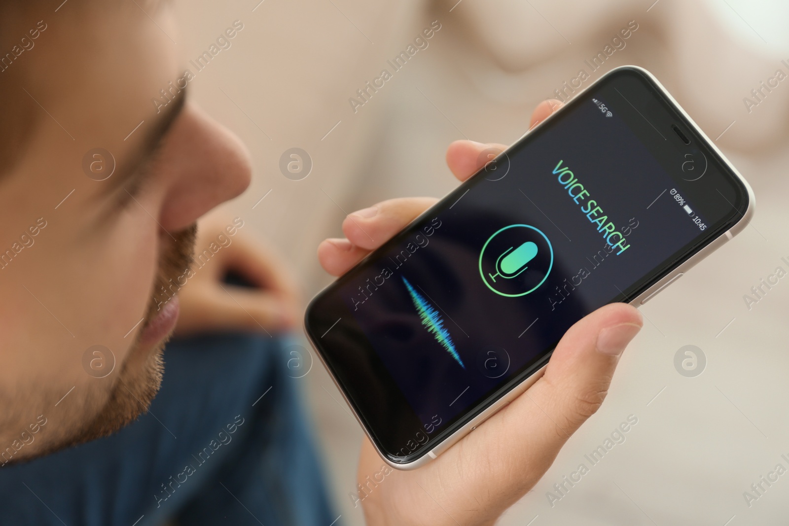 Photo of Young man using voice search on smartphone indoors, closeup