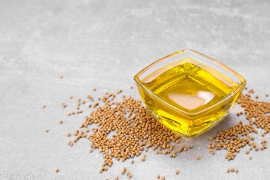 Photo of Bowl of natural oil and mustard seeds on light grey table. Space for text