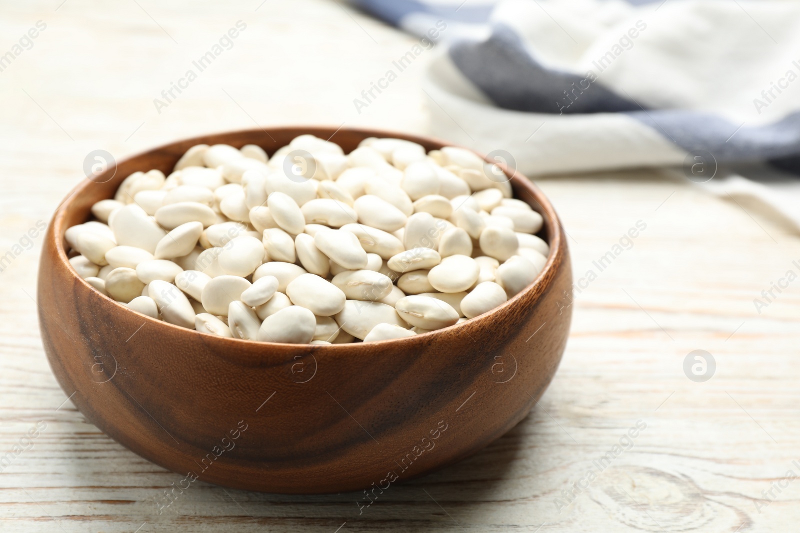 Photo of Bowl of uncooked white beans on wooden table, closeup