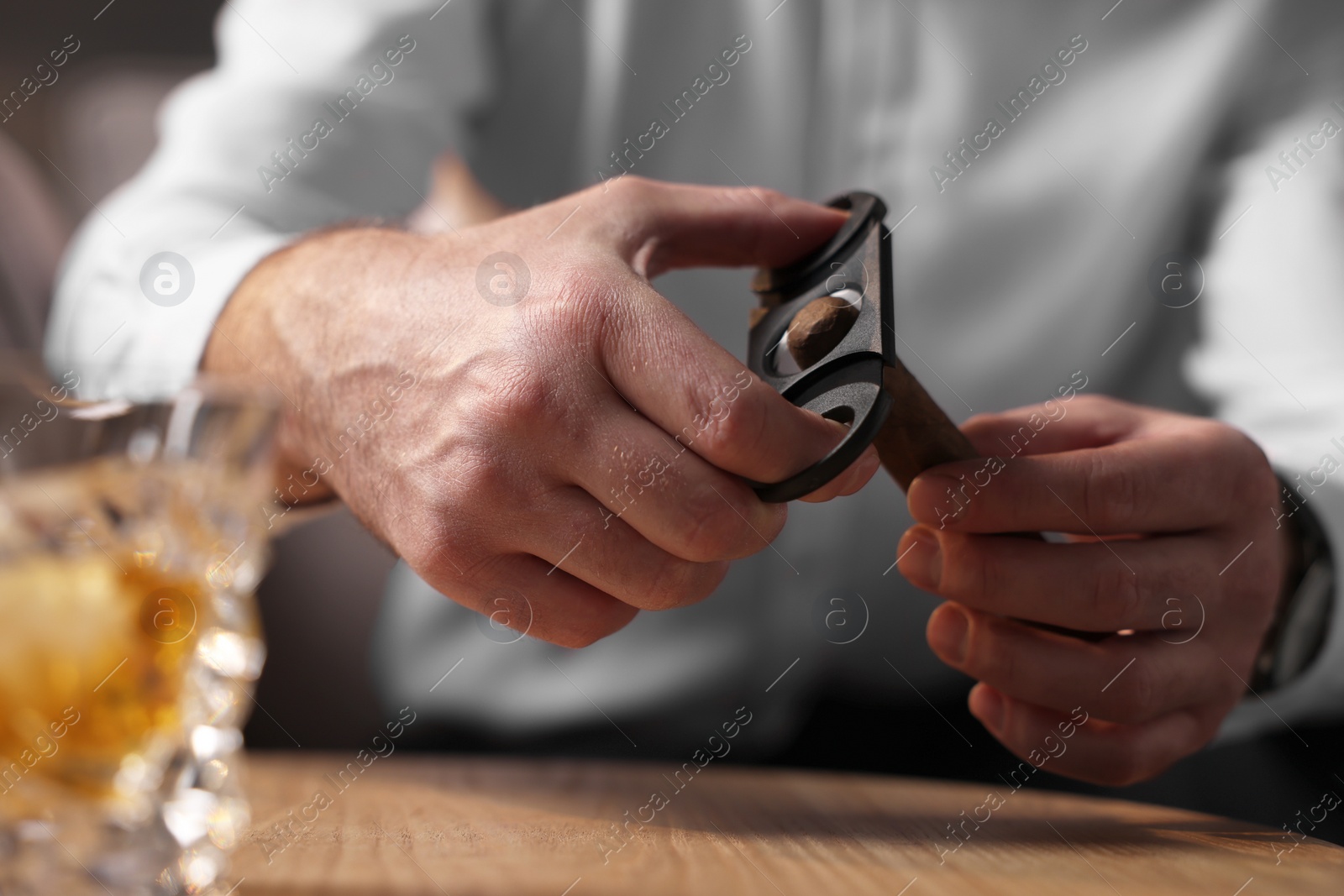 Photo of Man cutting tip of cigar at wooden table, closeup