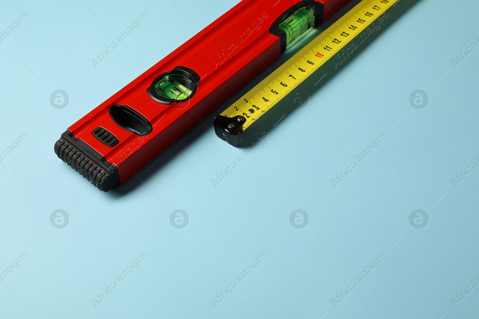 Photo of Building level and tape measure on light blue background. Space for text