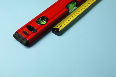 Photo of Building level and tape measure on light blue background. Space for text