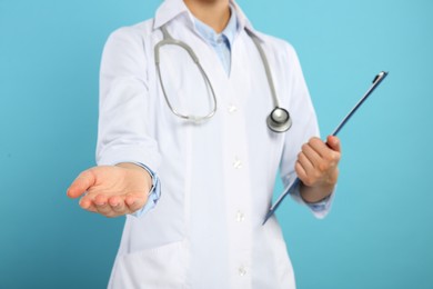 Photo of Doctor with stethoscope and clipboard holding something on light blue background, closeup