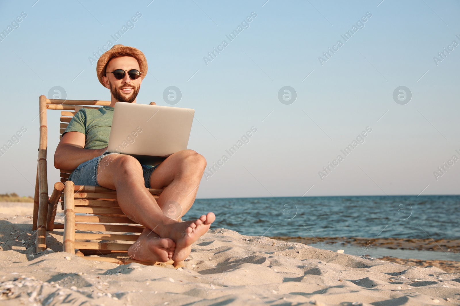 Photo of Man working with laptop in deck chair on beach. Space for text