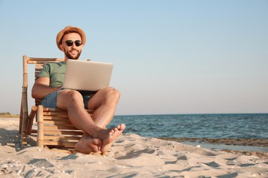 Photo of Man working with laptop in deck chair on beach. Space for text