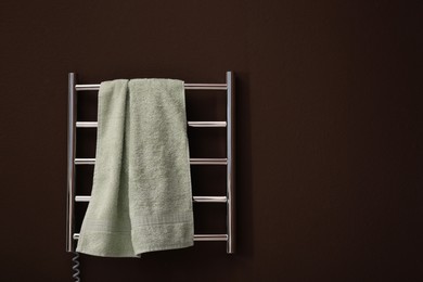 Photo of Modern heated towel rail with warm soft towel on brown wall. Space for text