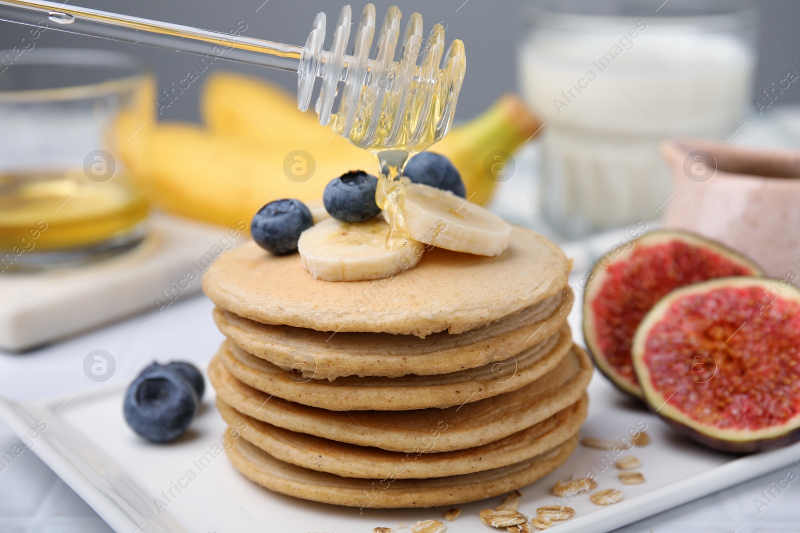 Photo of Pouring honey onto tasty oatmeal pancakes, closeup