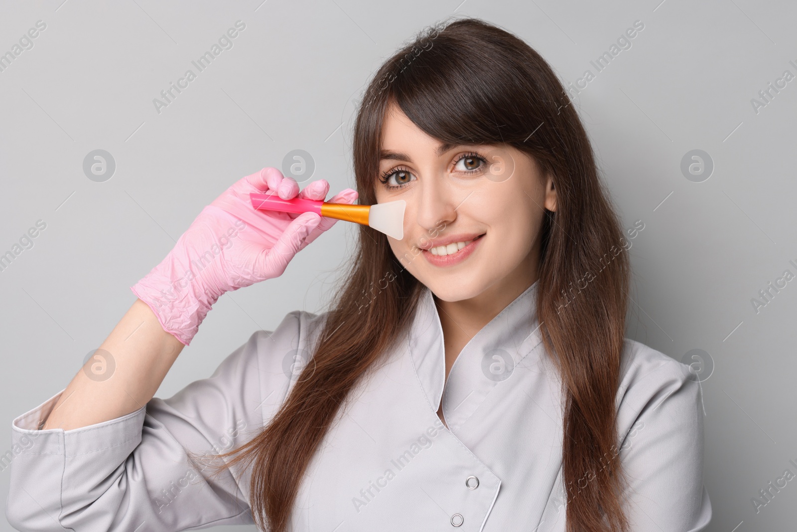 Photo of Cosmetologist with silicone cosmetic brush on grey background