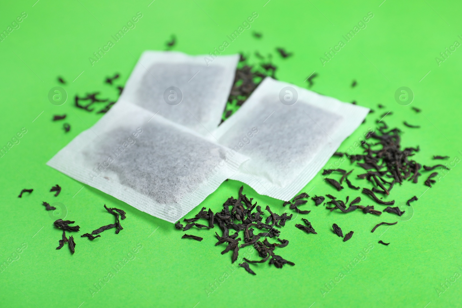 Photo of Tea bags with scattered dry leaves on color background