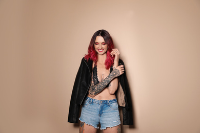 Photo of Beautiful woman with tattoos on body against beige background