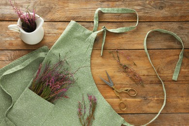 Photo of Clean apron with beautiful flowers on wooden table, flat lay