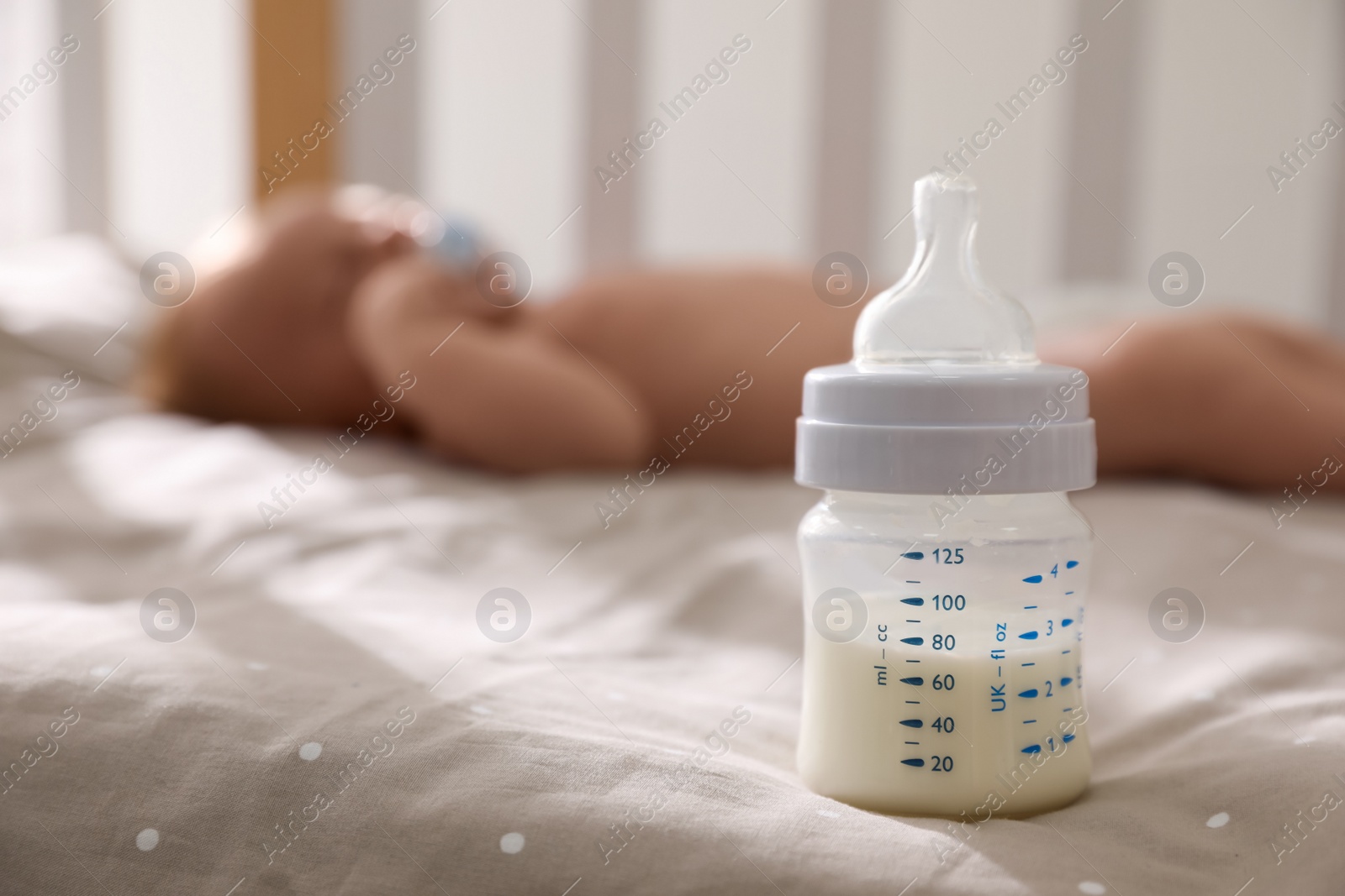 Photo of Healthy baby sleeping in cot, focus on bottle with milk