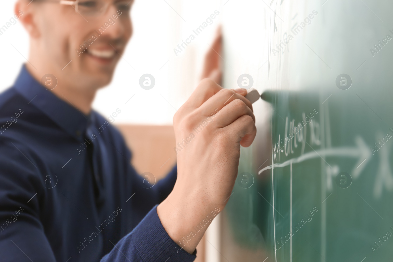 Photo of Young male teacher writing on blackboard in classroom