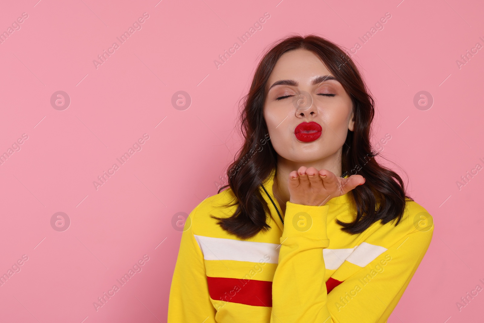 Photo of Beautiful young woman blowing kiss on pink background. Space for text