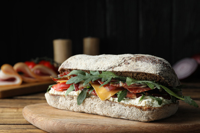 Photo of Delicious sandwich with fresh vegetables and prosciutto on wooden table