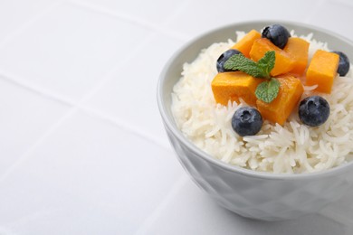 Photo of Bowl of delicious rice porridge with blueberries and pumpkin on white table, closeup. Space for text