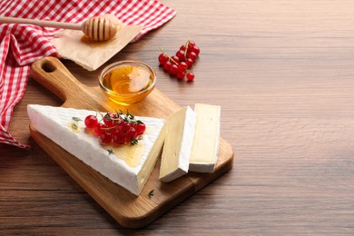 Photo of Brie cheese served with red currants and honey on wooden table. Space for text