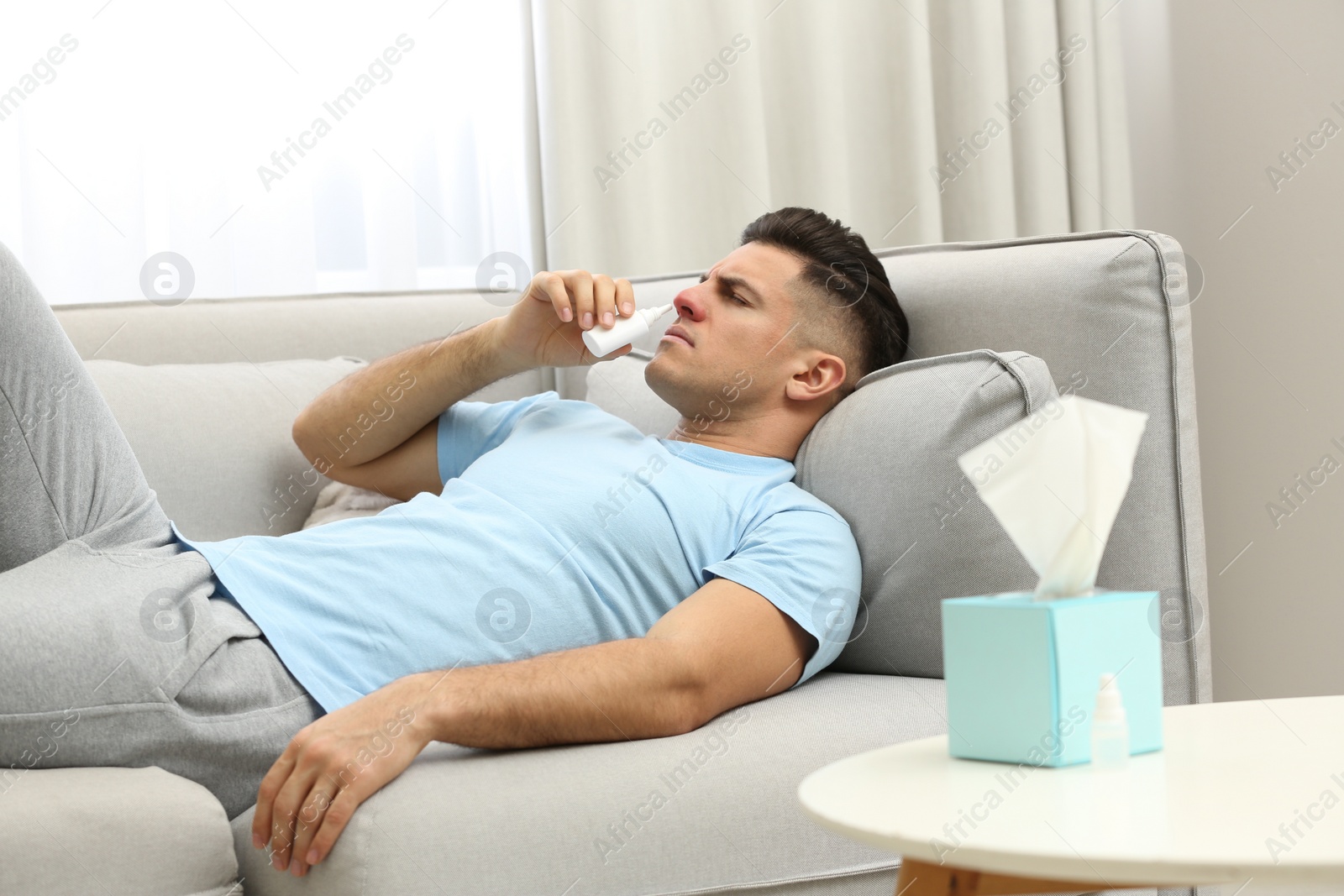 Photo of Ill man using nasal spray on sofa at home