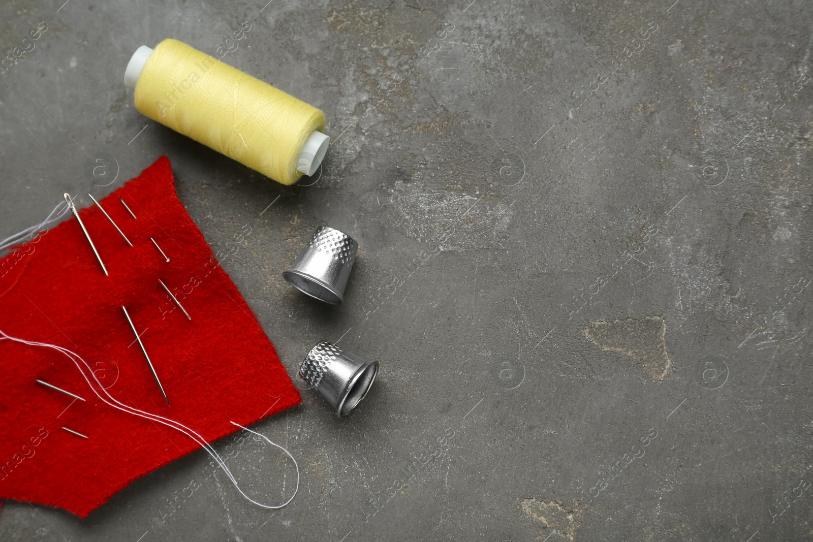 Photo of Thimbles, needles and thread on grey table, flat lay with space for text. Sewing accessories