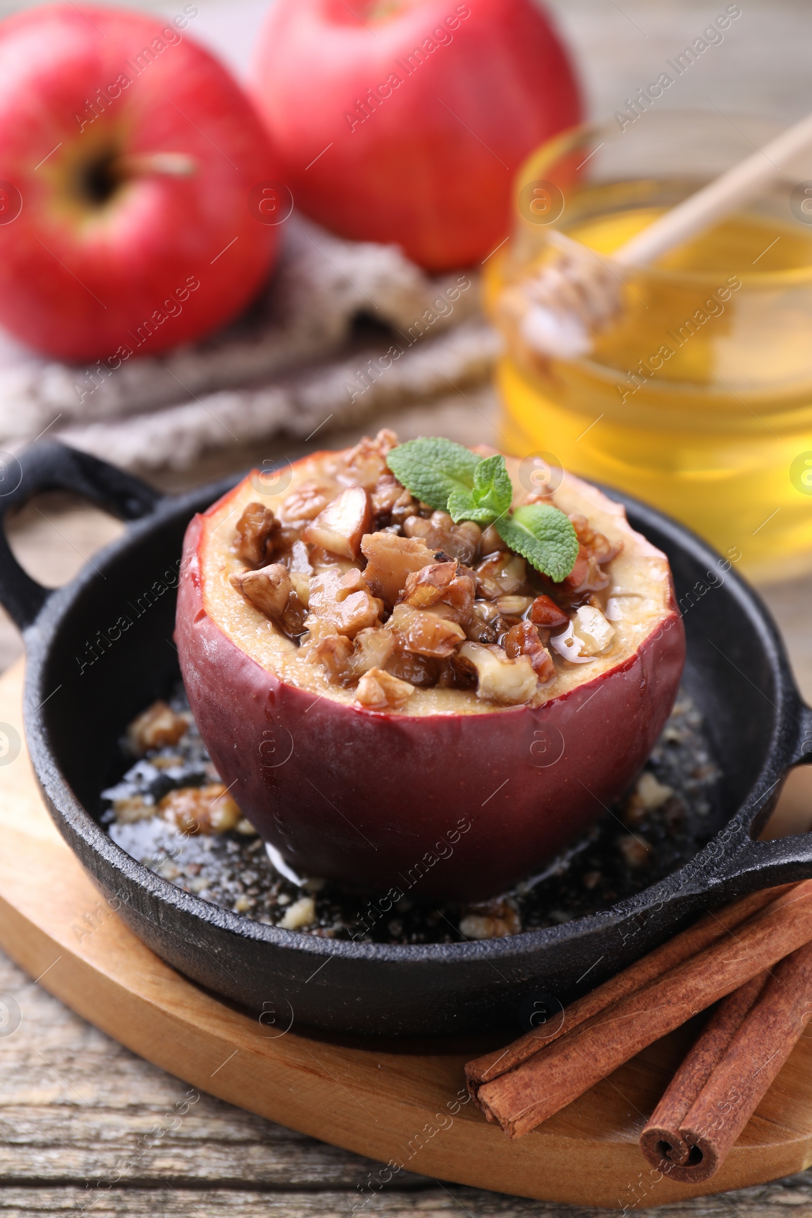 Photo of Tasty baked apple with nuts, honey and mint in baking dish on wooden table