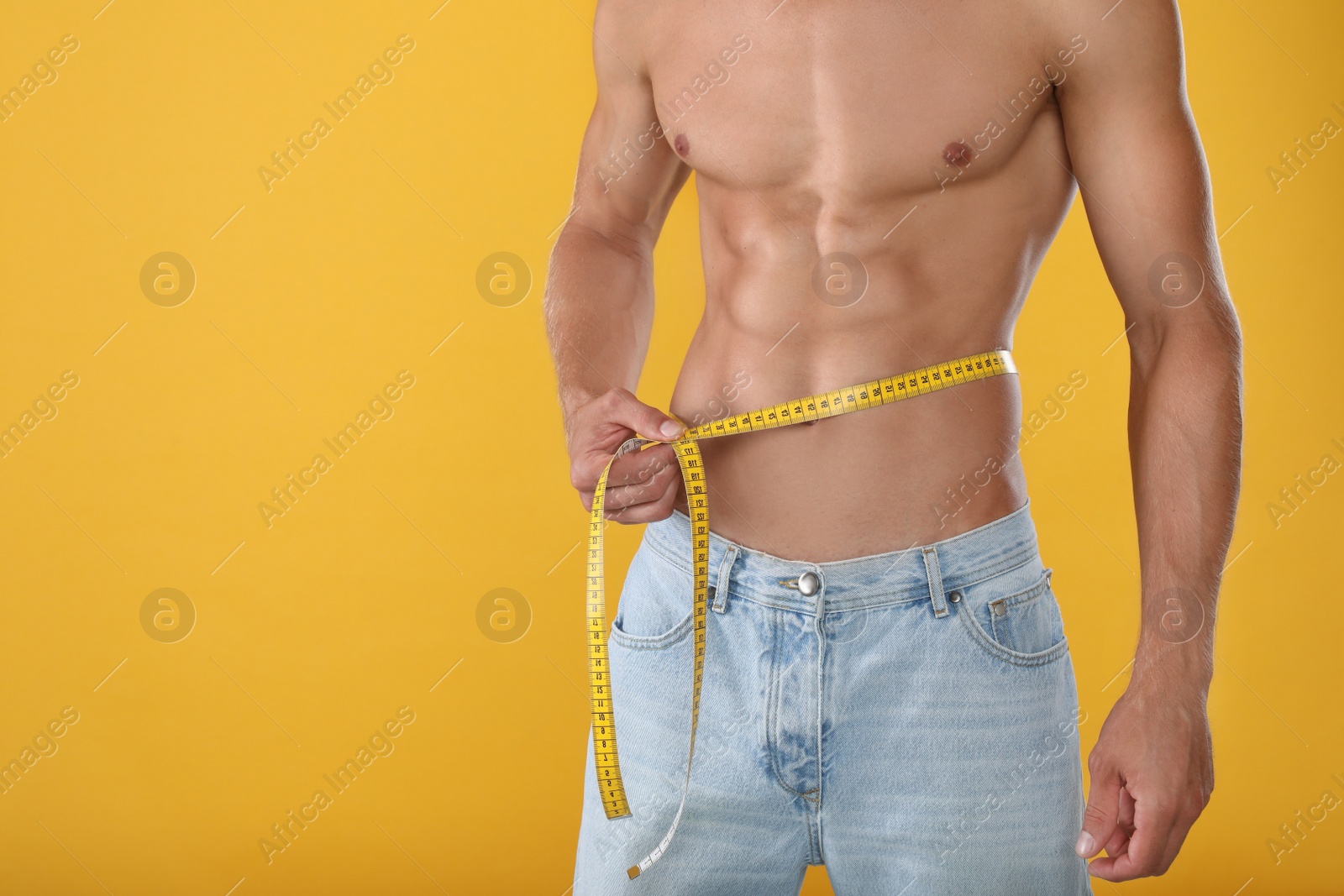 Photo of Shirtless man with slim body and measuring tape around his waist on yellow background, closeup. Space for text