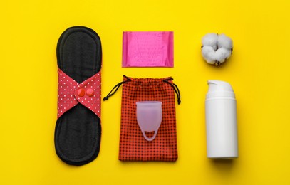 Cloth menstrual pad and other female hygiene products on yellow background, flat lay