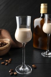 Photo of Coffee cream liqueur in glasses, bottle and beans on black wooden table