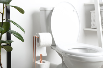 Photo of Holder with paper rolls near toilet bowl in bathroom