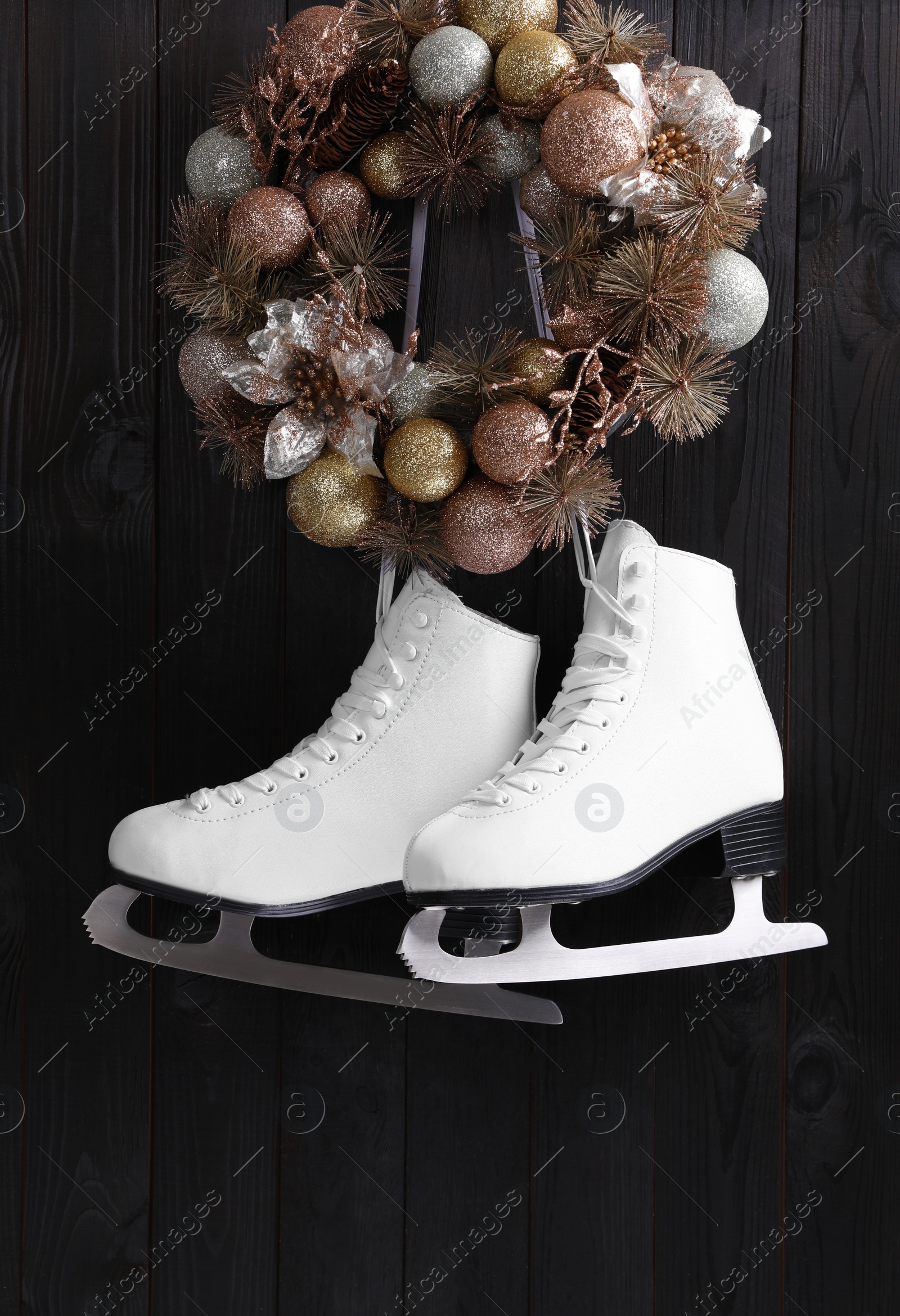 Photo of Pair of ice skates and beautiful Christmas wreath hanging on dark wooden wall