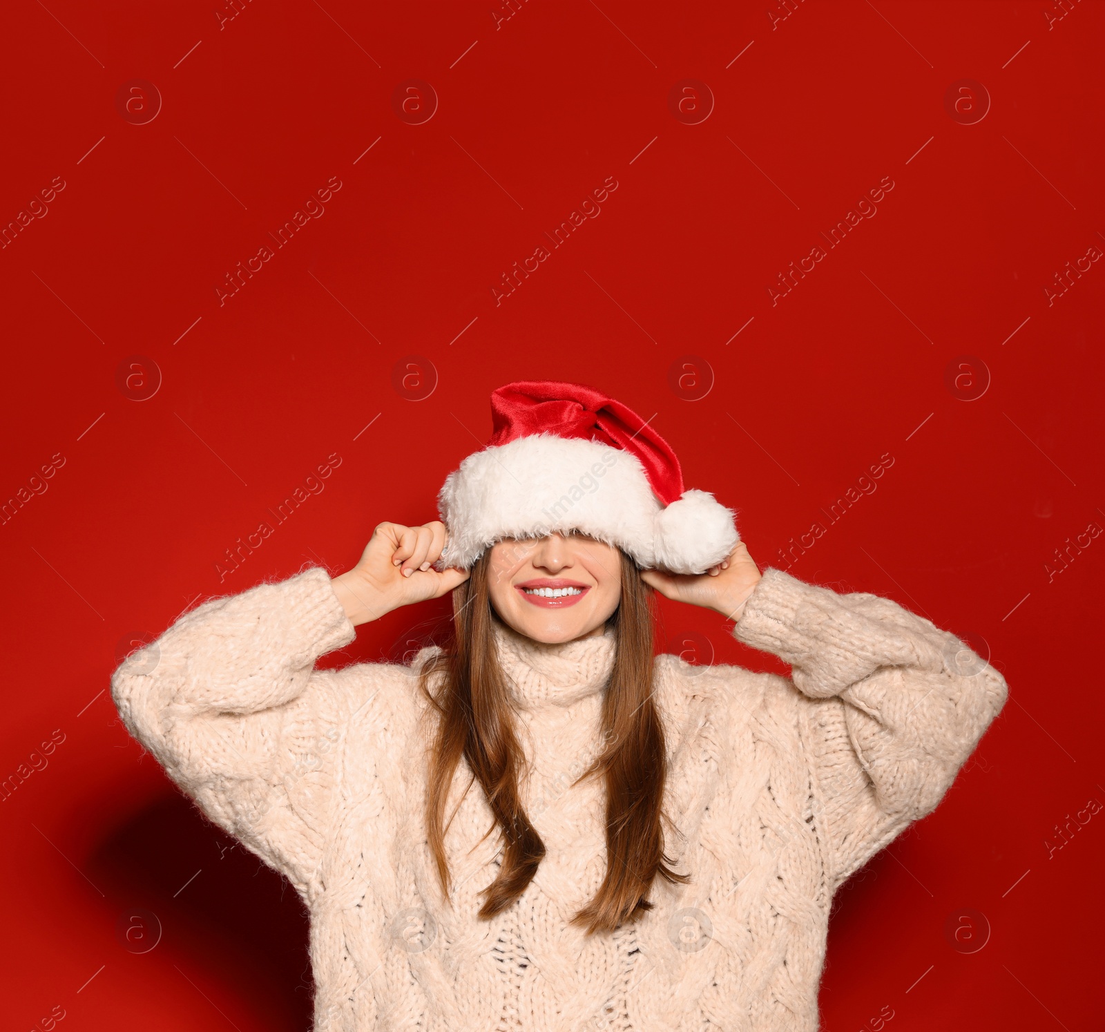 Photo of Young woman in Christmas sweater and Santa hat on red background