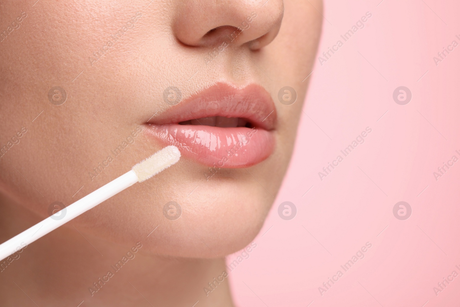 Photo of Woman applying lip gloss on pink background, closeup. Space for text