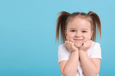 Photo of Portrait of cute little girl on light blue background, space for text