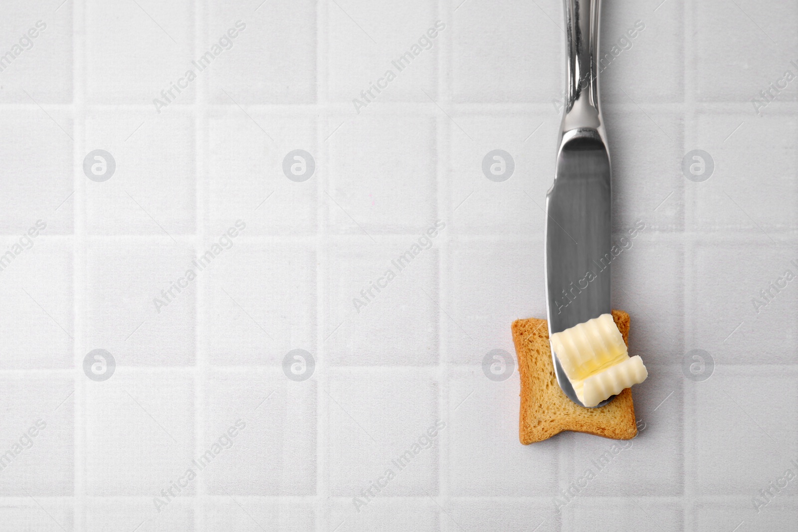 Photo of Tasty butter curl, knife and piece of dry bread on white tiled table, top view. Space for text